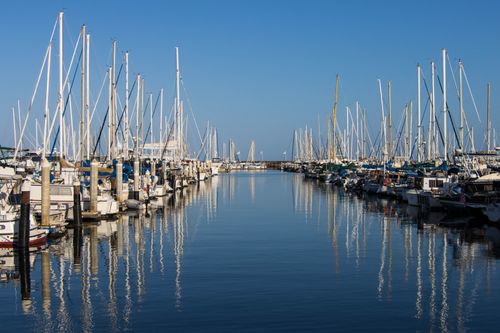 Free A tranquil marina scene with sailboats reflected in calm water and a clear blue sky. Stock Photo