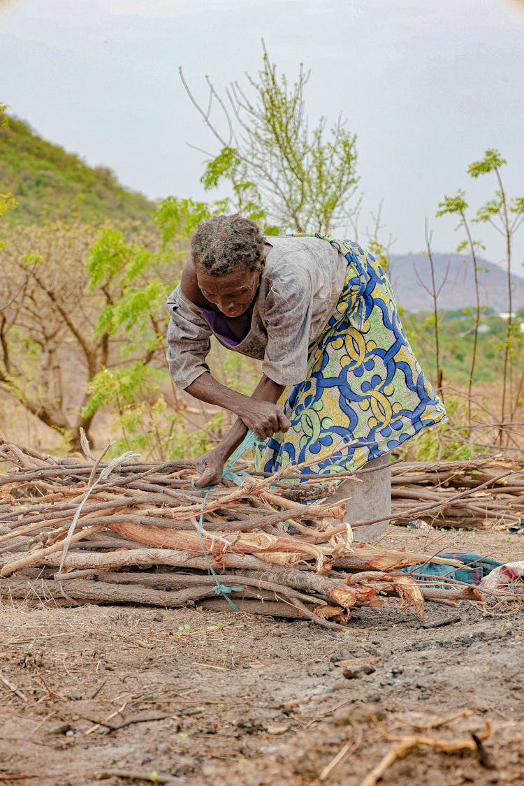 Woman Tying A Bundle Of Sticks On A Field 