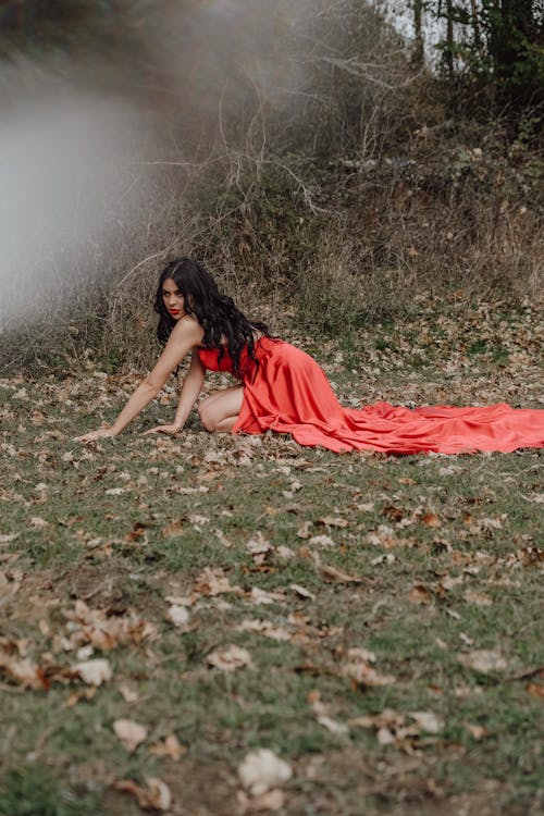 Young Brunette in a Red Dress Sitting on the Ground Outdoors 
