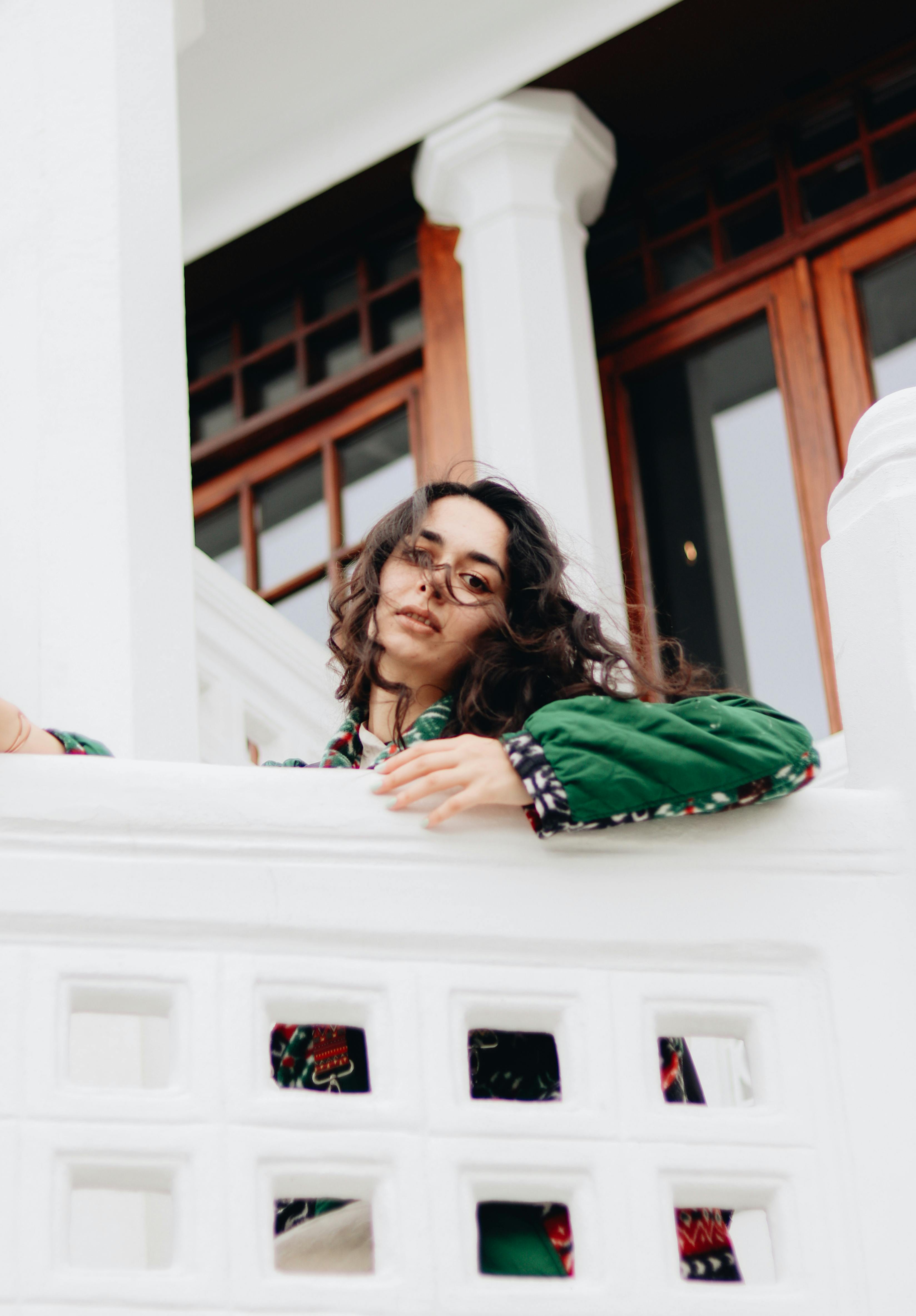 Stylish woman in a green jacket enjoying a moment of relaxation on a marble balcony.