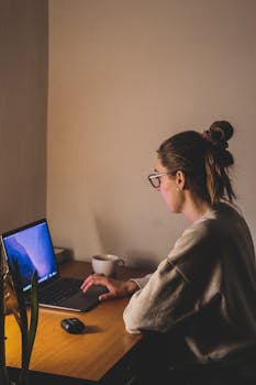 A woman concentrating at a laptop in a warm-lit London workspace, embodying productivity.