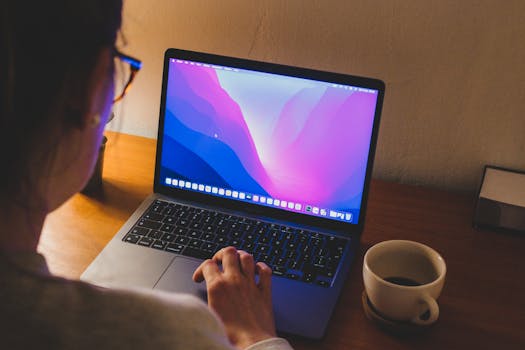 A woman working on a laptop with a coffee cup beside her, in a cozy indoor setting.