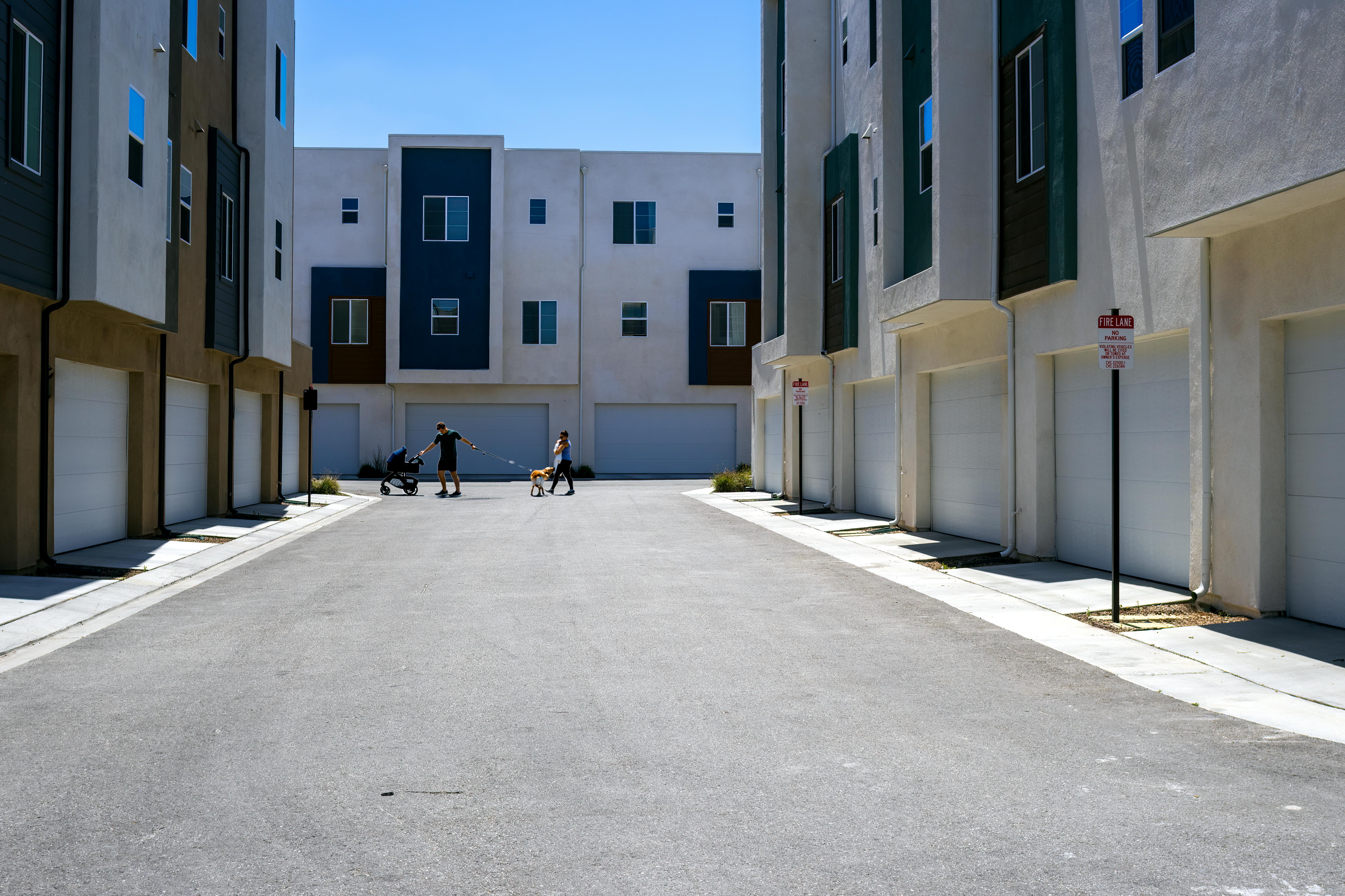 A quiet urban alley framed by sleek modern residential buildings under a summer sky.