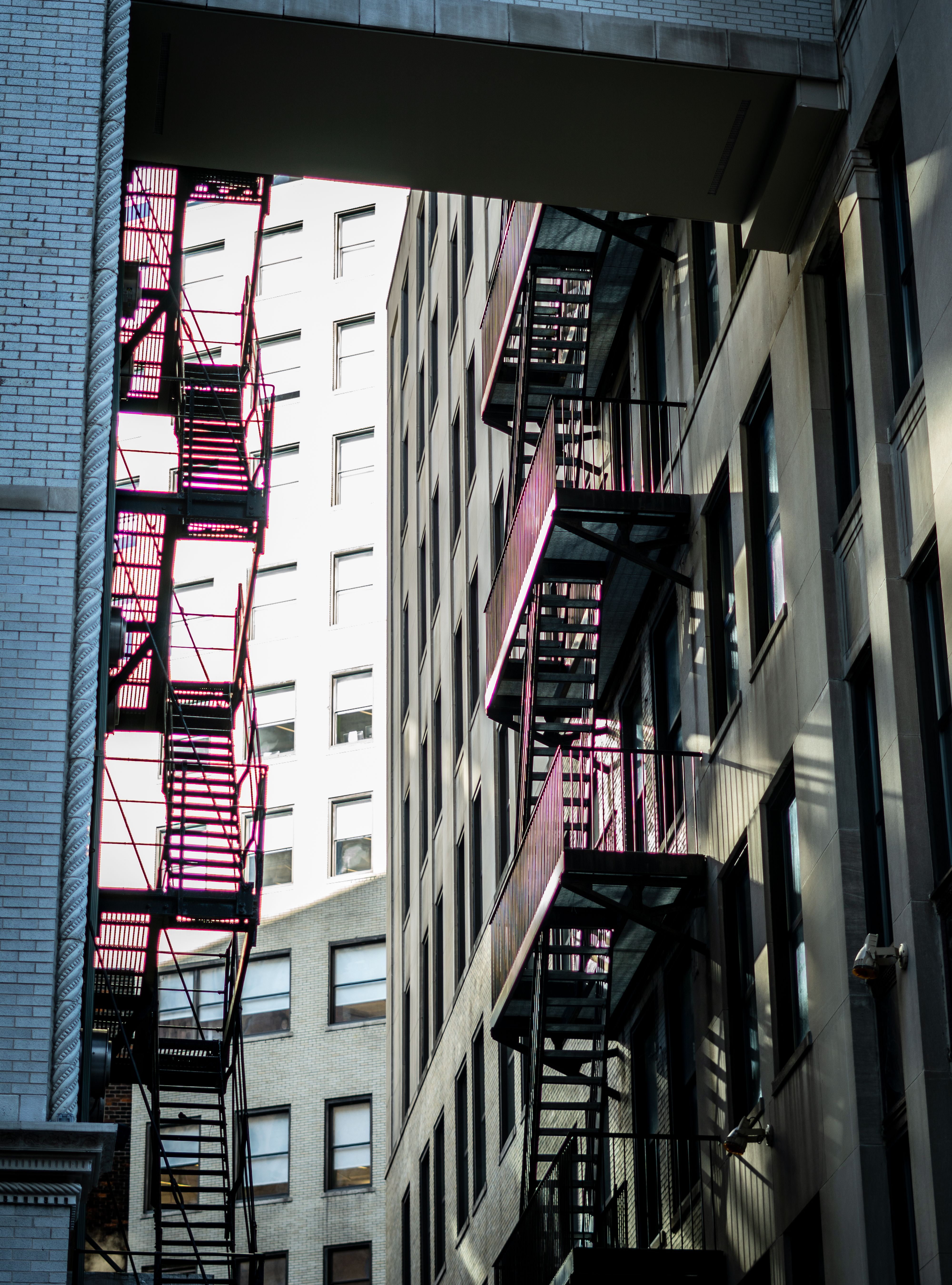 Sunlit urban buildings featuring fire escapes creating a striking architectural pattern.