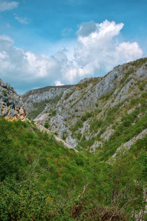 Free Scenic view of a lush green valley surrounded by rocky mountains under a blue sky with clouds in Bosnia and Herzegovina. Stock Photo