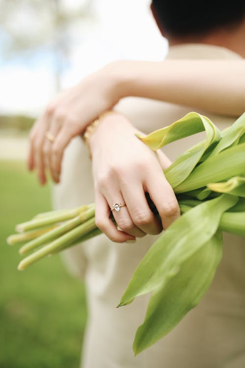 Free Close-up of a couple embracing with a bouquet of green tulips highlighting an engagement ring. Stock Photo