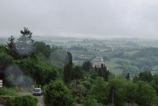 A misty landscape with Santa Maria della Consolazione in Todi, Italy amidst lush green hills and trees.