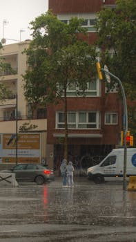 Pedestrians in raincoats crossing a wet urban street during a downpour.