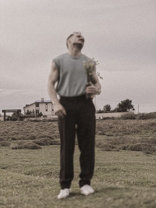 Free A man stands joyously in the countryside holding wildflowers, showcasing nature's beauty. Stock Photo
