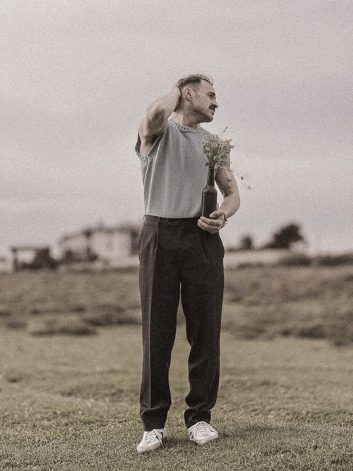 Free Man standing in a grassy field holding a bottle with flowers on a cloudy day. Stock Photo