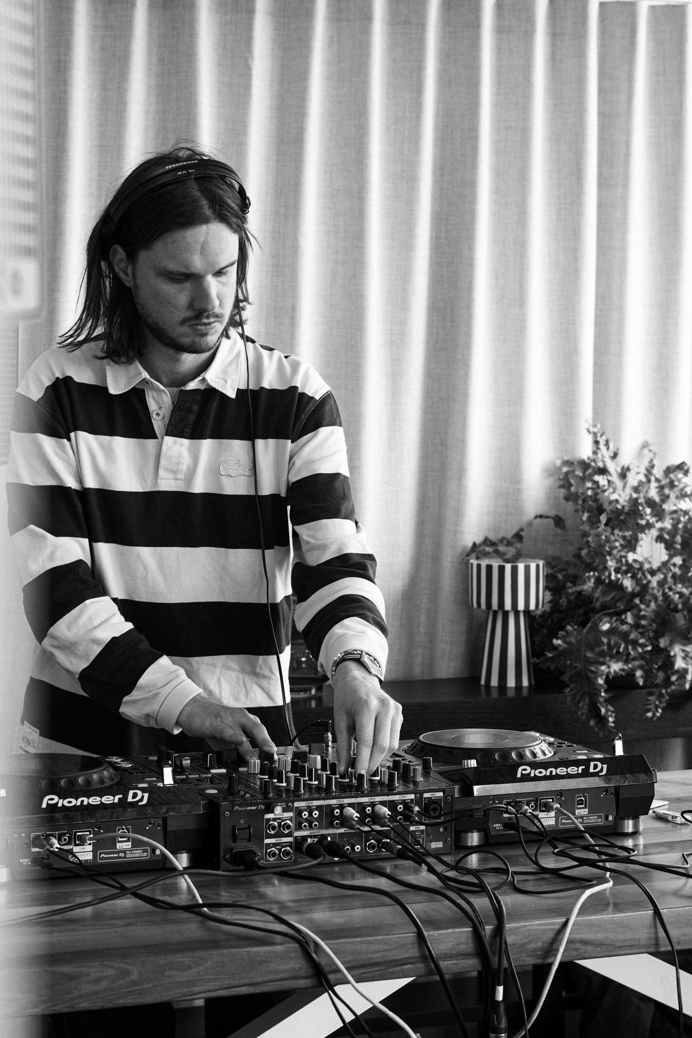 Black and white portrait of a DJ mixing music indoors, focusing on the equipment.