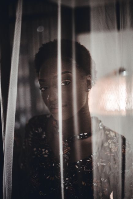 Elegant portrait of a woman standing behind a sheer curtain, exuding mystery and grace.