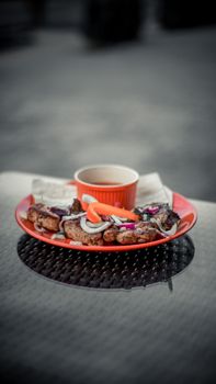 Close-up of grilled meat with onions on a vibrant plate, paired with a dipping sauce, outdoors.