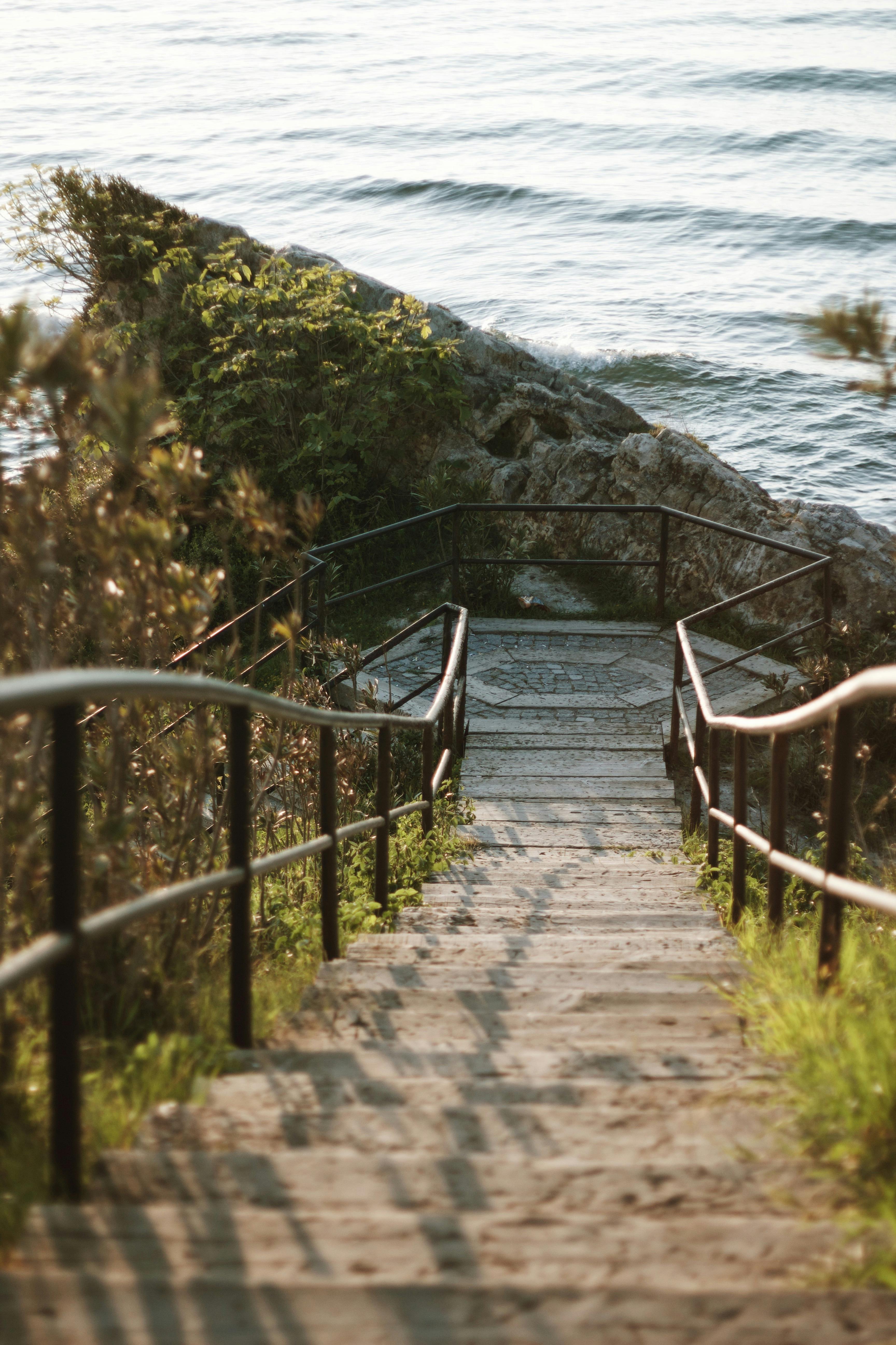 Wooden stairs leading to a peaceful beach with calming waves and lush greenery.