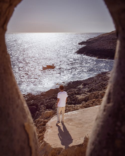 Man Standing on Sunlit Rocks on Sea Shore