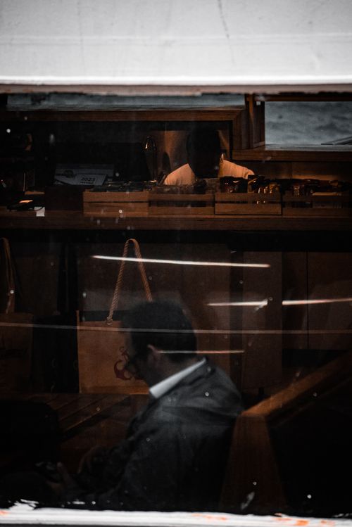Free A man with short hair sits quietly inside a train, with reflections of an interior view visible through the window. Stock Photo