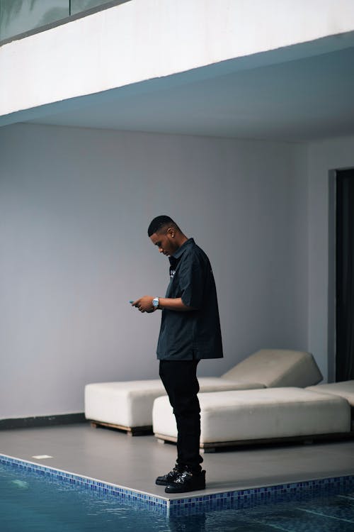 A young man standing by a pool using a phone to manipulate its smart technology.