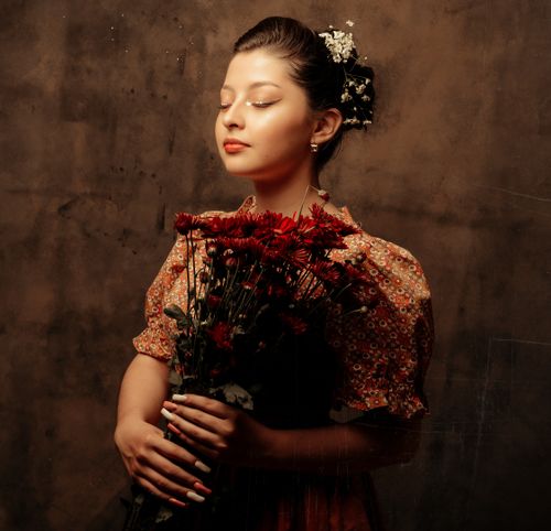 Free A woman with an updo hairstyle elegantly poses with a bouquet of red flowers in a studio setting. Stock Photo