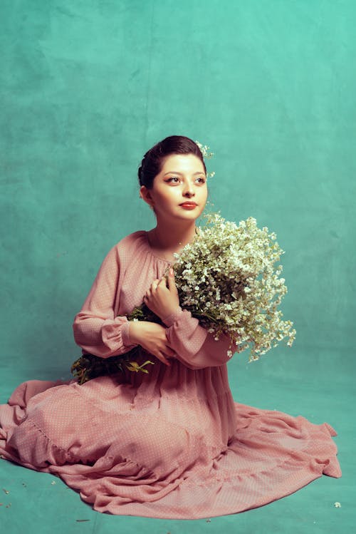 Young Woman in a Pink Dress and a Bunch of Flowers Sitting on the Floor 