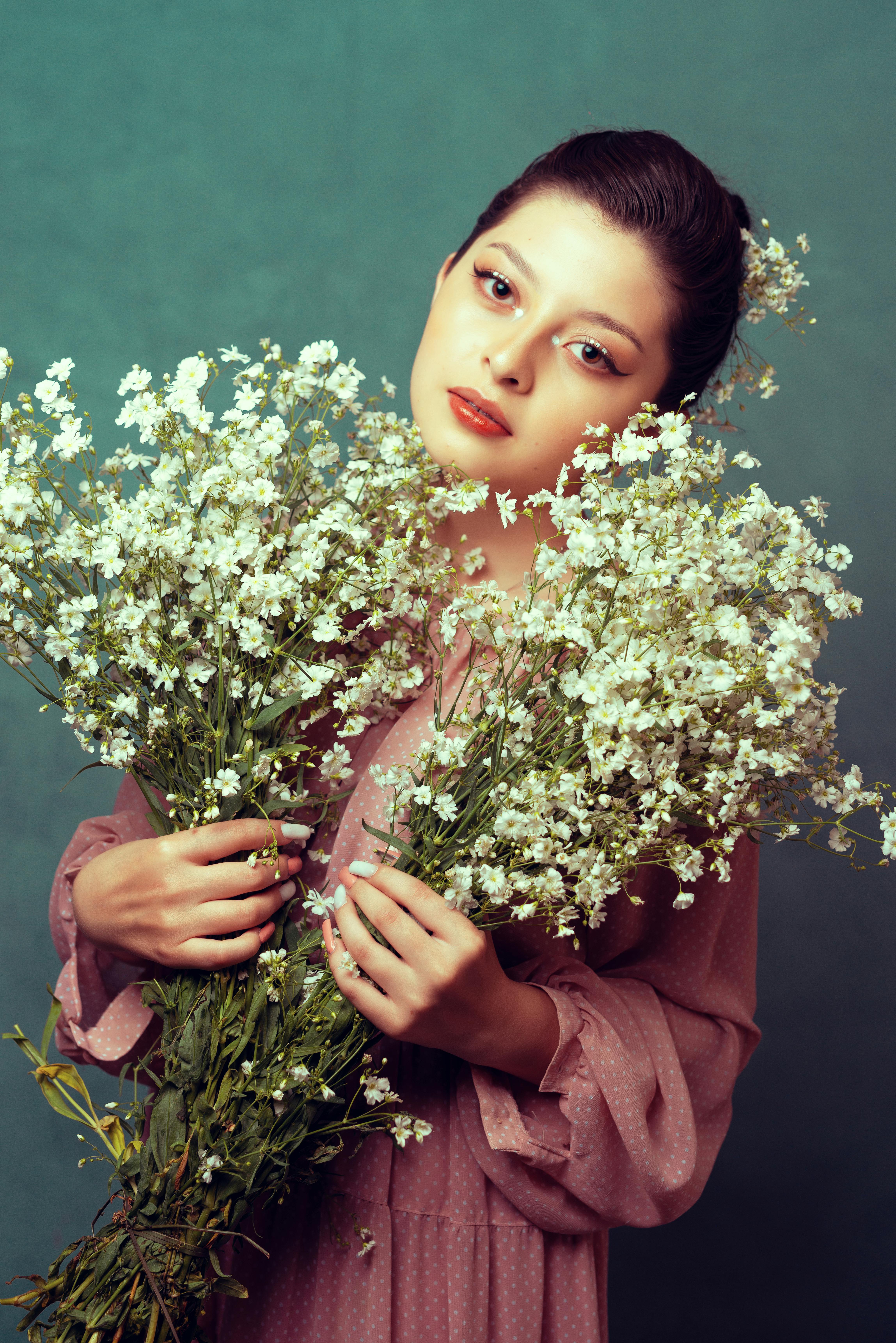 Portrait of a woman elegantly holding white flowers against a green backdrop in a studio setting.