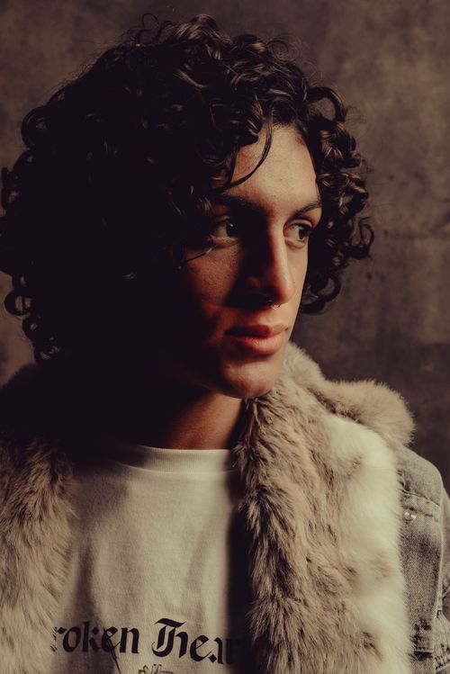 Free Moody portrait of a young man with curly hair wearing a fur jacket in a studio setting. Stock Photo