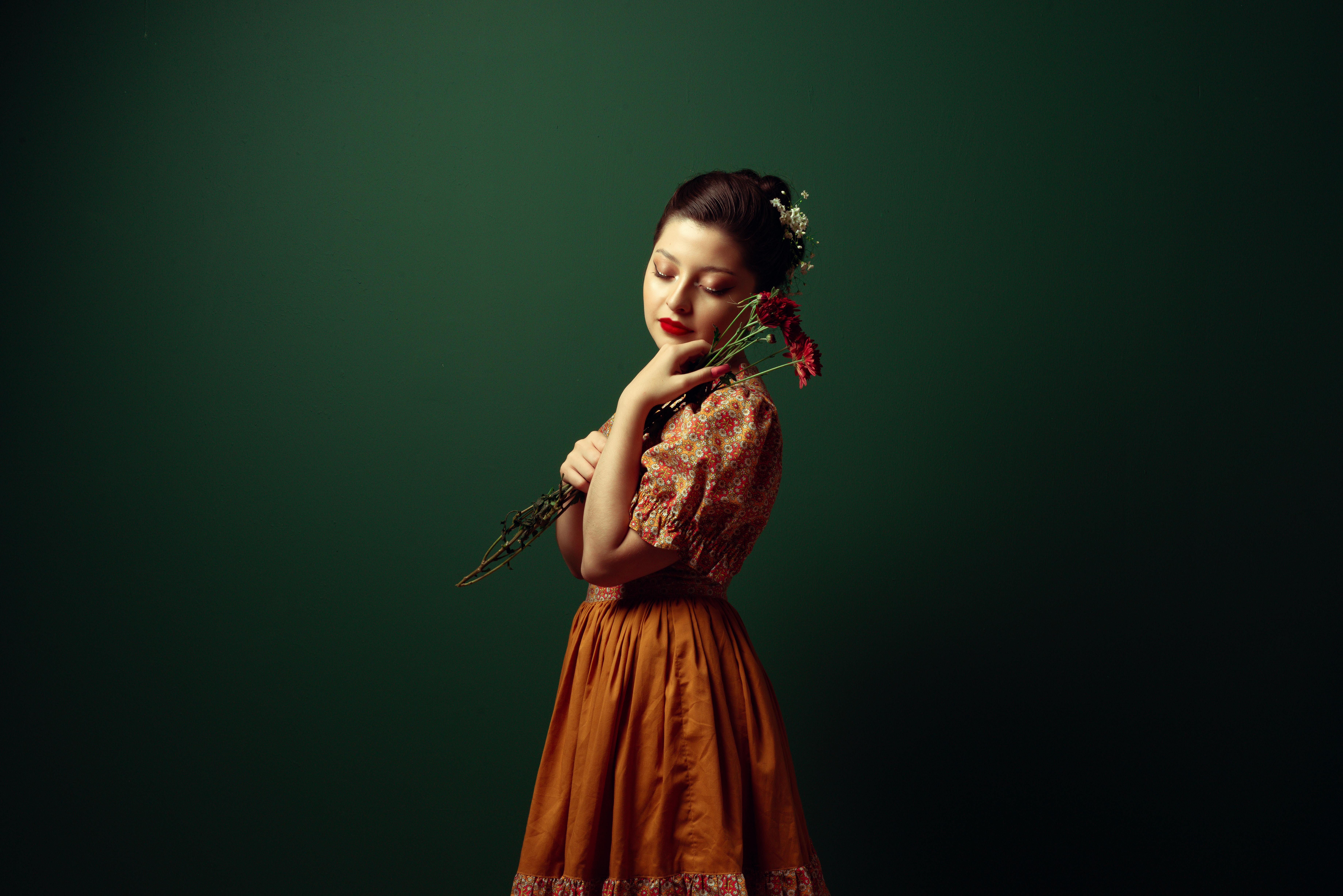 Portrait of a woman with closed eyes holding flowers, wearing a vintage dress, in a studio setting.