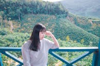 一位年轻女子若有所思地站在阳台上，俯瞰着郁郁葱葱的青山