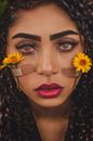 Close-up portrait of a woman with flowers and facial bandages, evoking emotions.