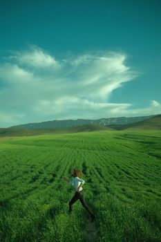 A man joyfully runs through a vast green field under a clear blue sky, symbolizing freedom and adventure.