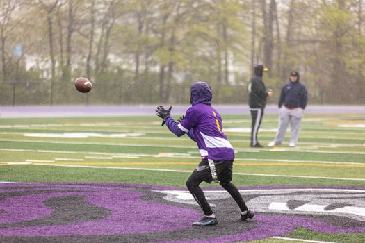 Athletes practicing rugby on a rainy outdoor field, wearing sportswear and training gear.