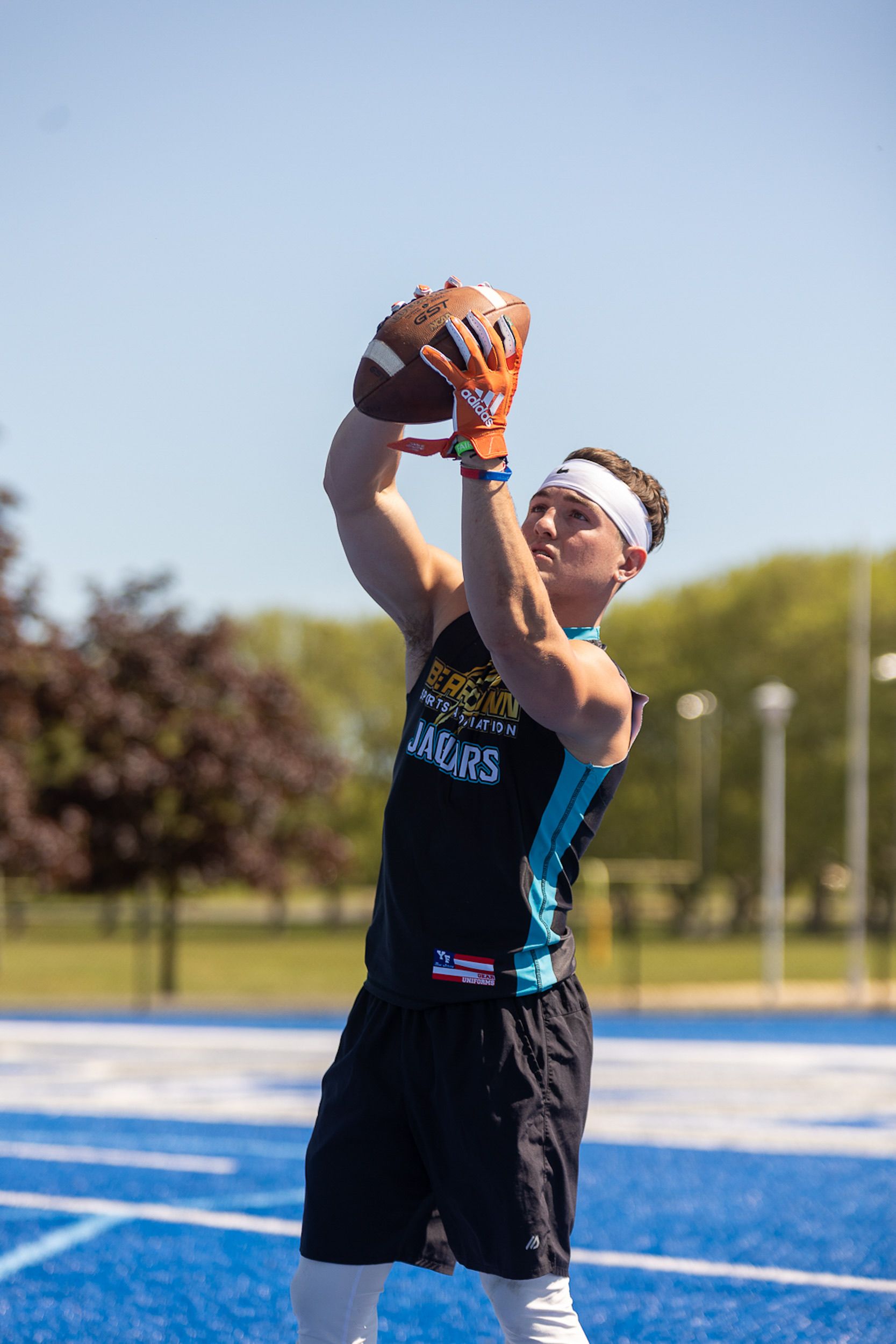 Young man catching a football on a blue sports field during a sunny day.