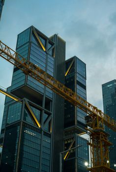 Dramatic view of contemporary skyscrapers with a construction crane set against a twilight sky.