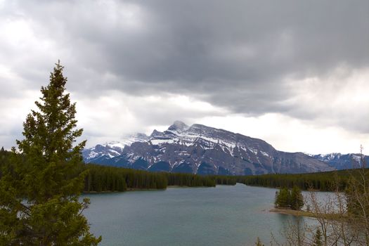 Snow-capped mountains under a cloudy sky, reflecting a serene lake scene.