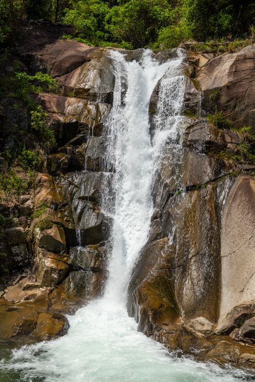 Free A stunning waterfall cascading over rocks surrounded by vibrant green foliage. Stock Photo