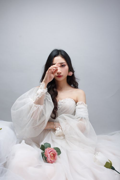 Free Young woman in a white tulle dress holding a pink rose in a studio setting. Stock Photo