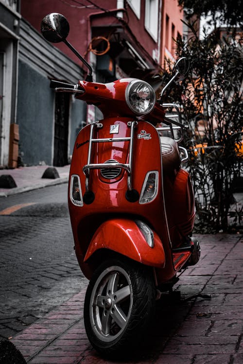 A Red Scooter Parked on the Sidewalk 