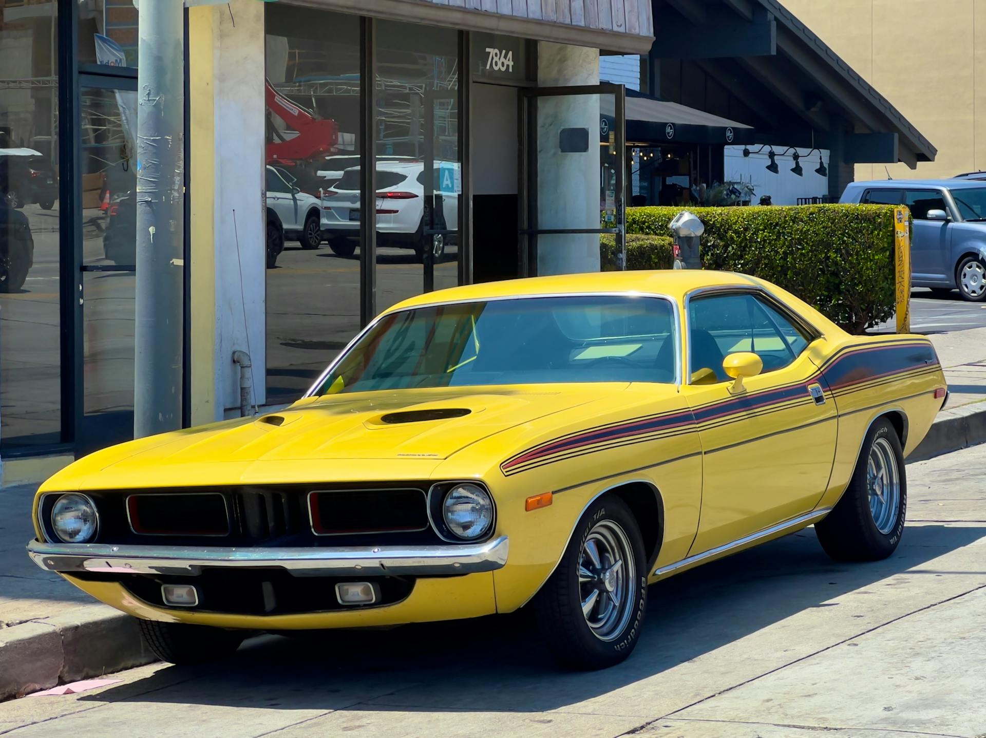 A vibrant yellow Plymouth Barracuda classic car parked on a city street, showcasing urban charm and vintage style.