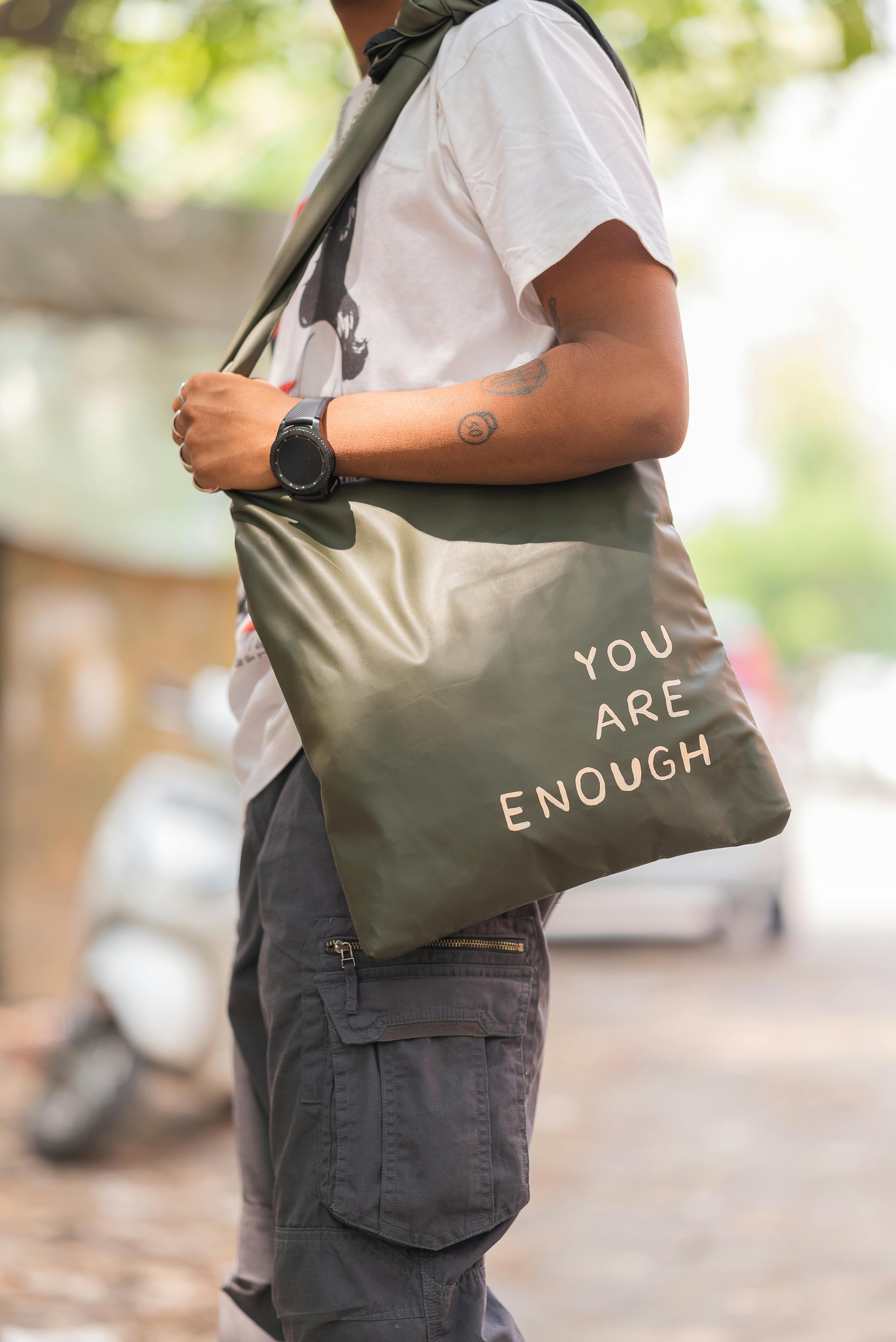 Man wearing casual outfit holding a motivational tote bag on city streets.