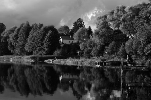 A peaceful scene of a person fishing by a serene lake surrounded by lush trees.