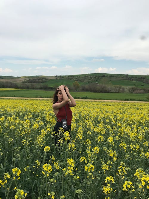 Woman Standing in the Rapeseed Field with a Camera on the Strap