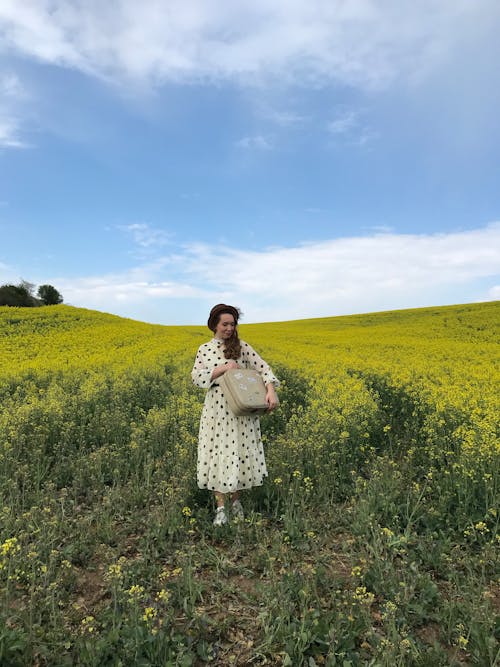Woman Standing in the Rapeseed Field with a Suitcase