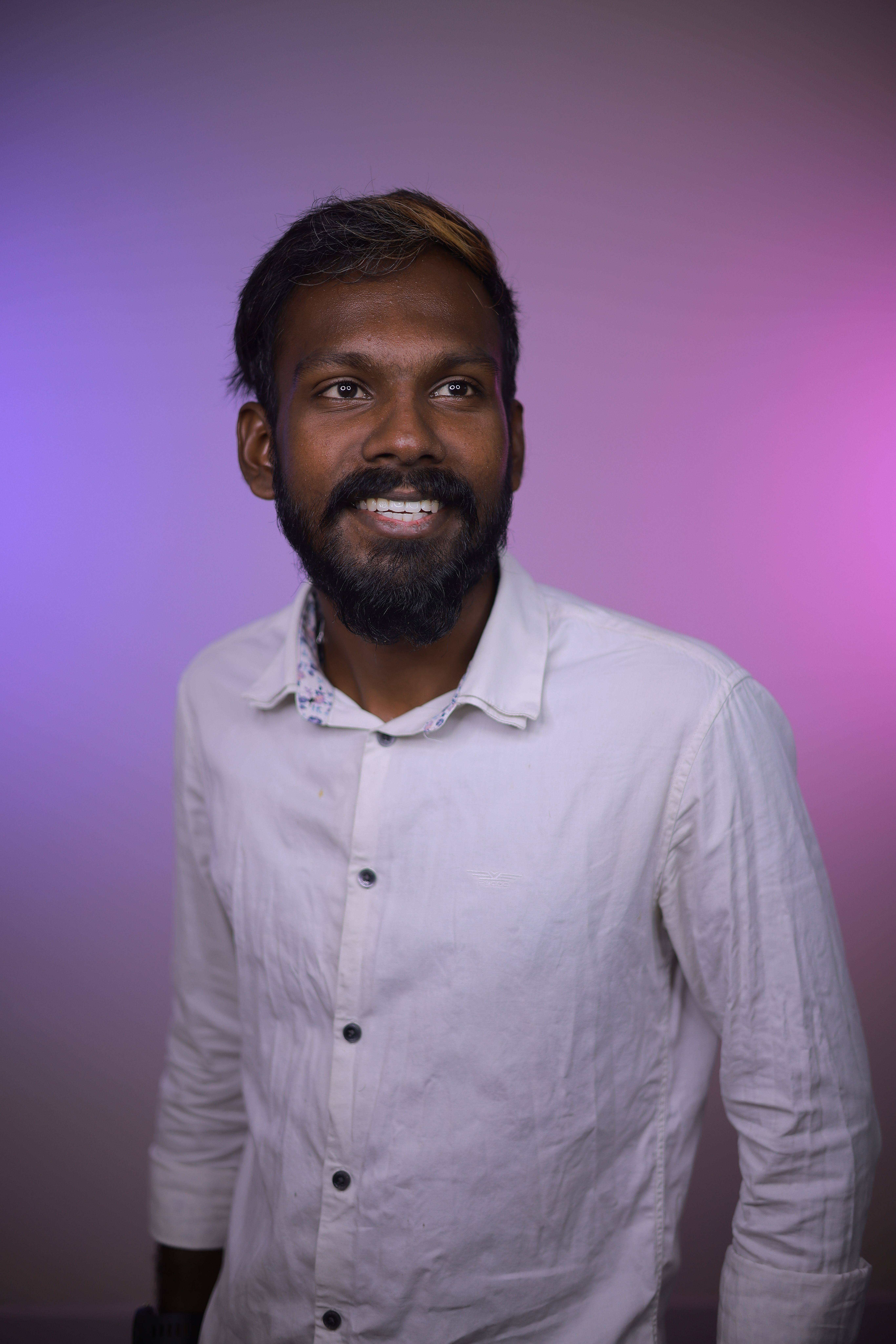Smiling man in white shirt with a beard standing against a colorful background.
