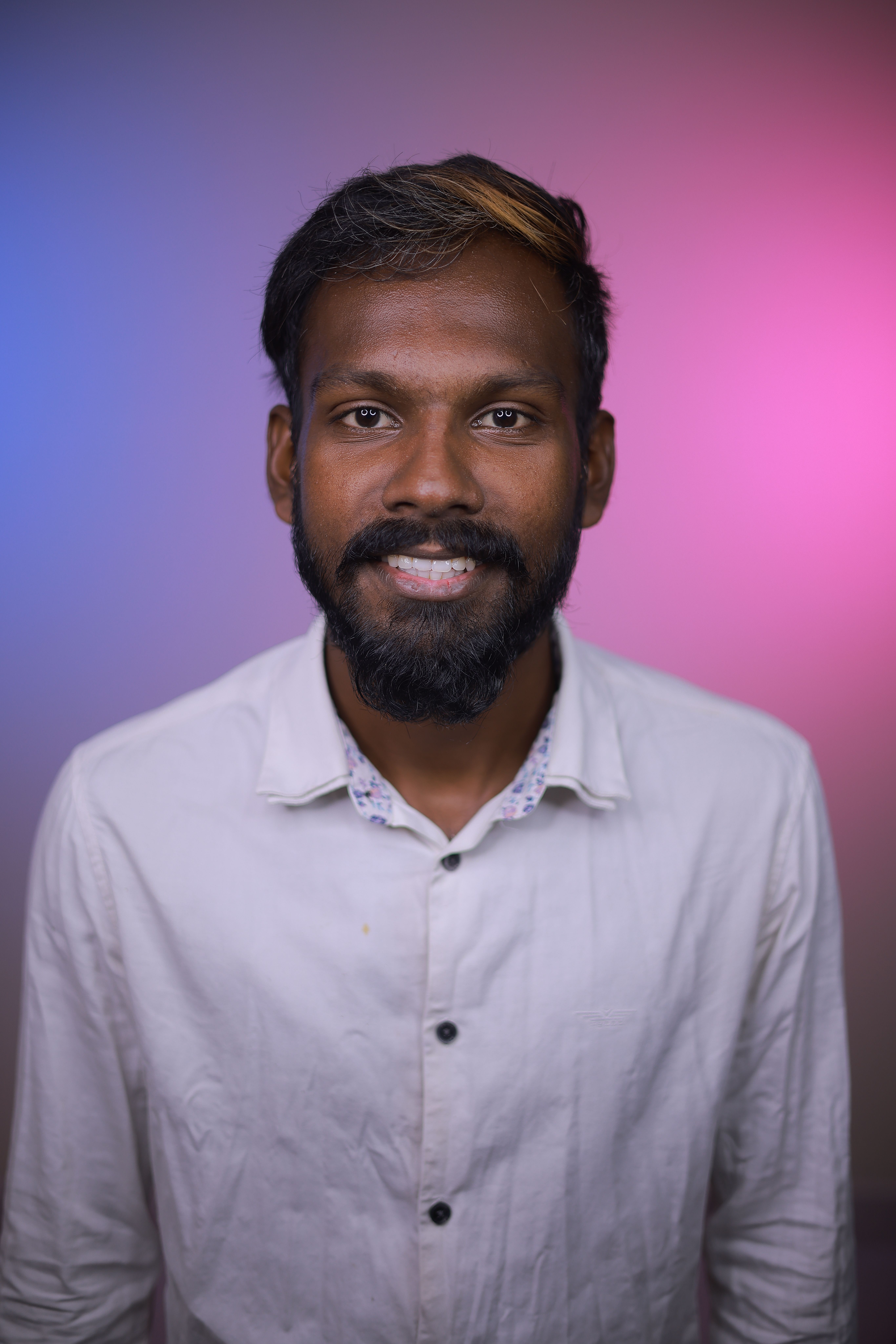 A confident man smiling against a gradient pink and blue background.