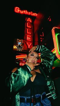 Woman posing in front of vibrant neon lights in a city alley at night.