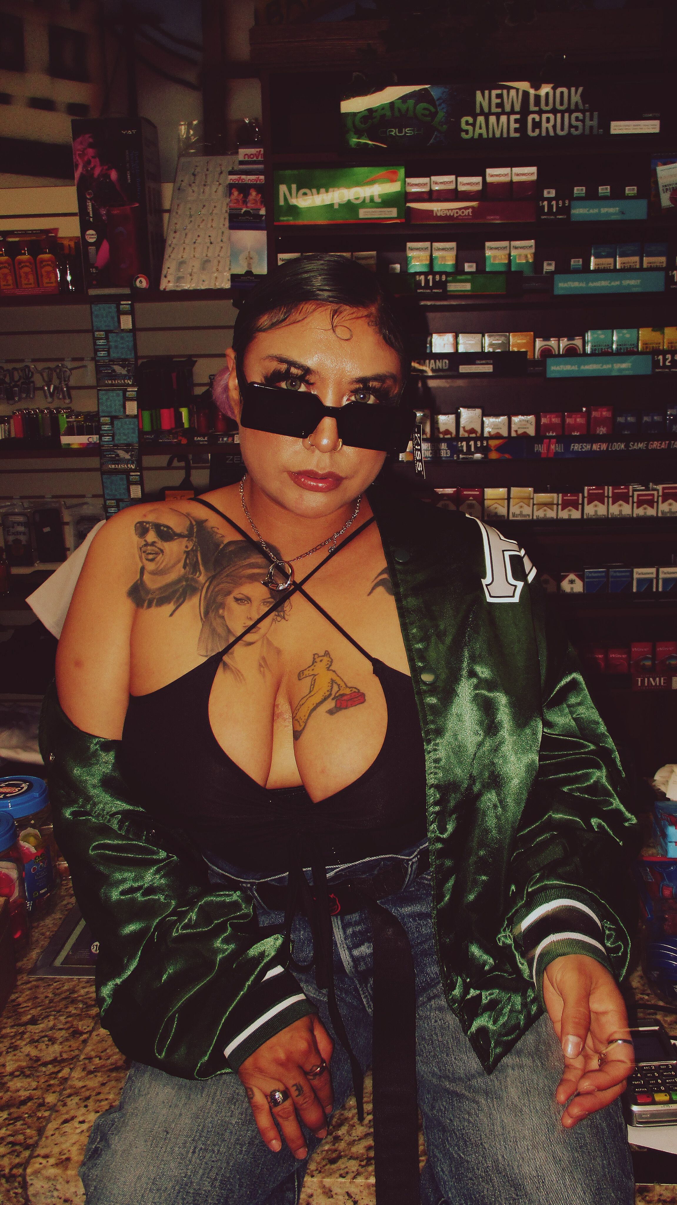 Confident woman with sunglasses and tattoos in a trendy urban store setting at night.