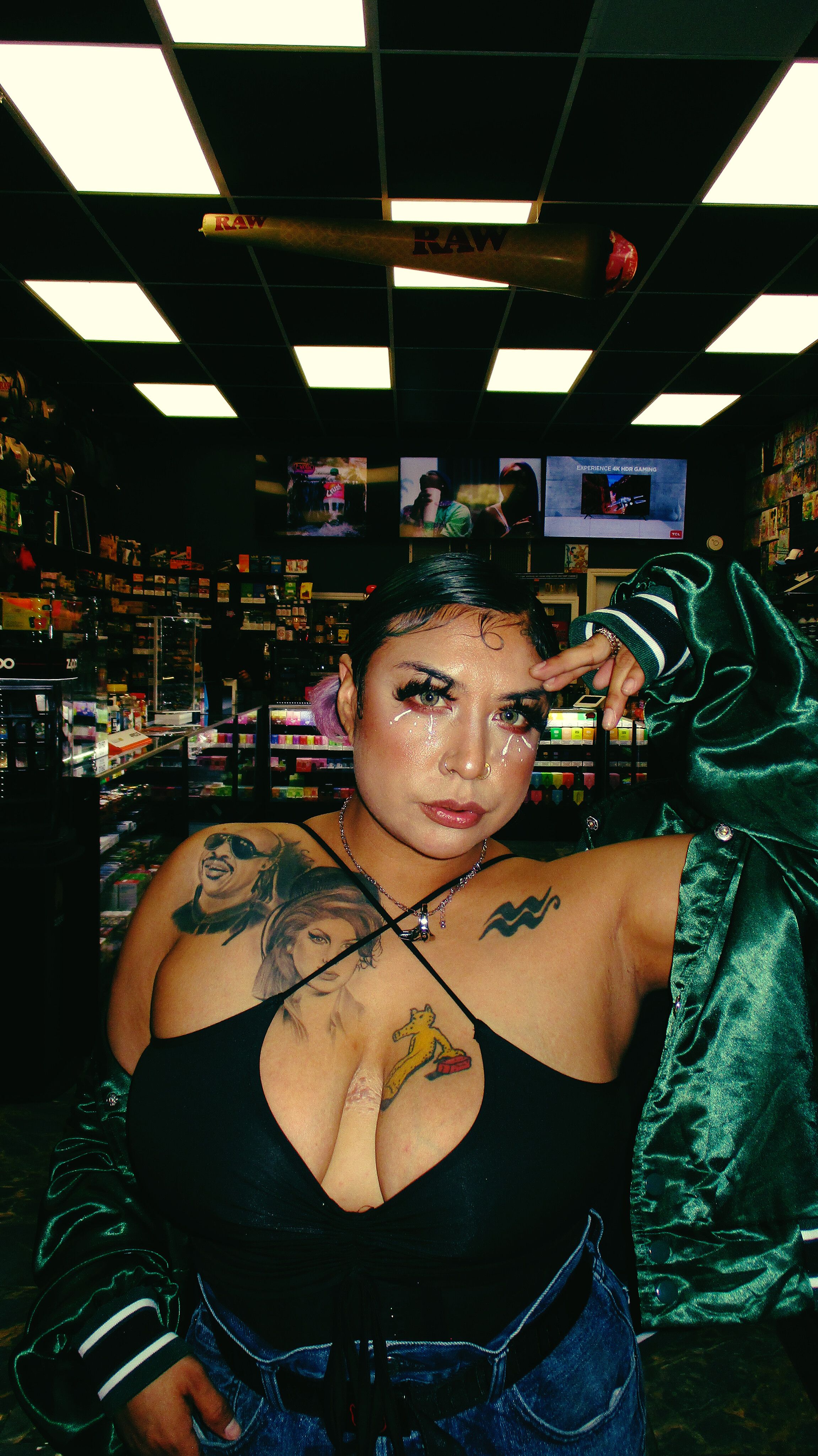 Stylish woman posing indoors with tattoos and fashion-forward makeup.