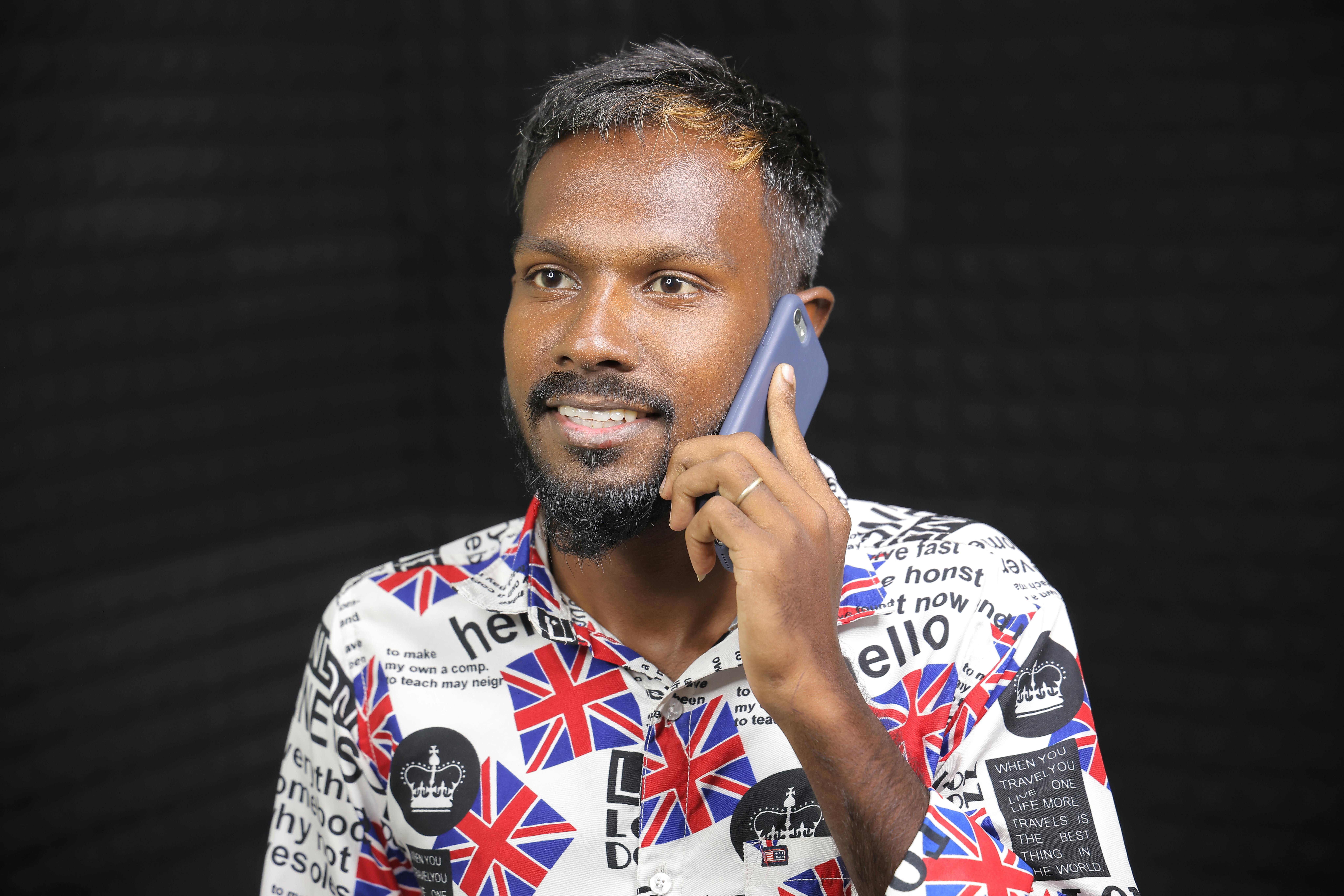 A South Asian man in a patterned shirt using a smartphone indoors.