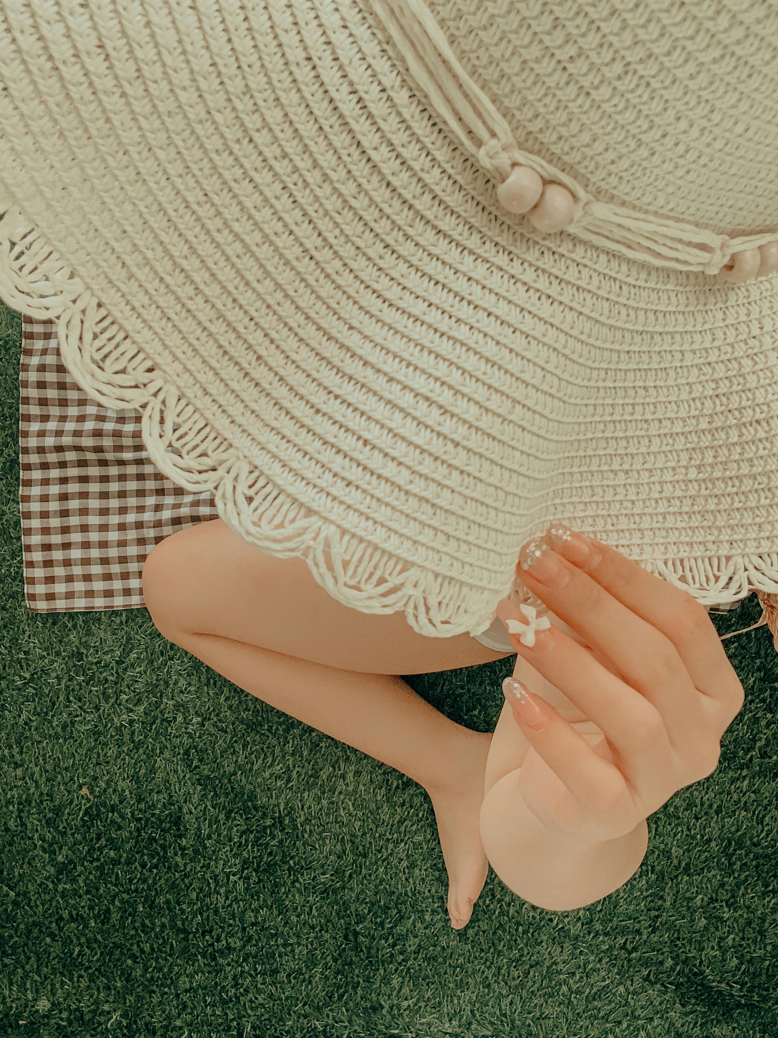 Top view of a woman enjoying a summer picnic, showcasing her acrylic nails and a stylish sunhat.