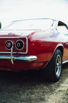 Elegant red vintage car parked outdoors, showcasing shiny chrome details and classic design.