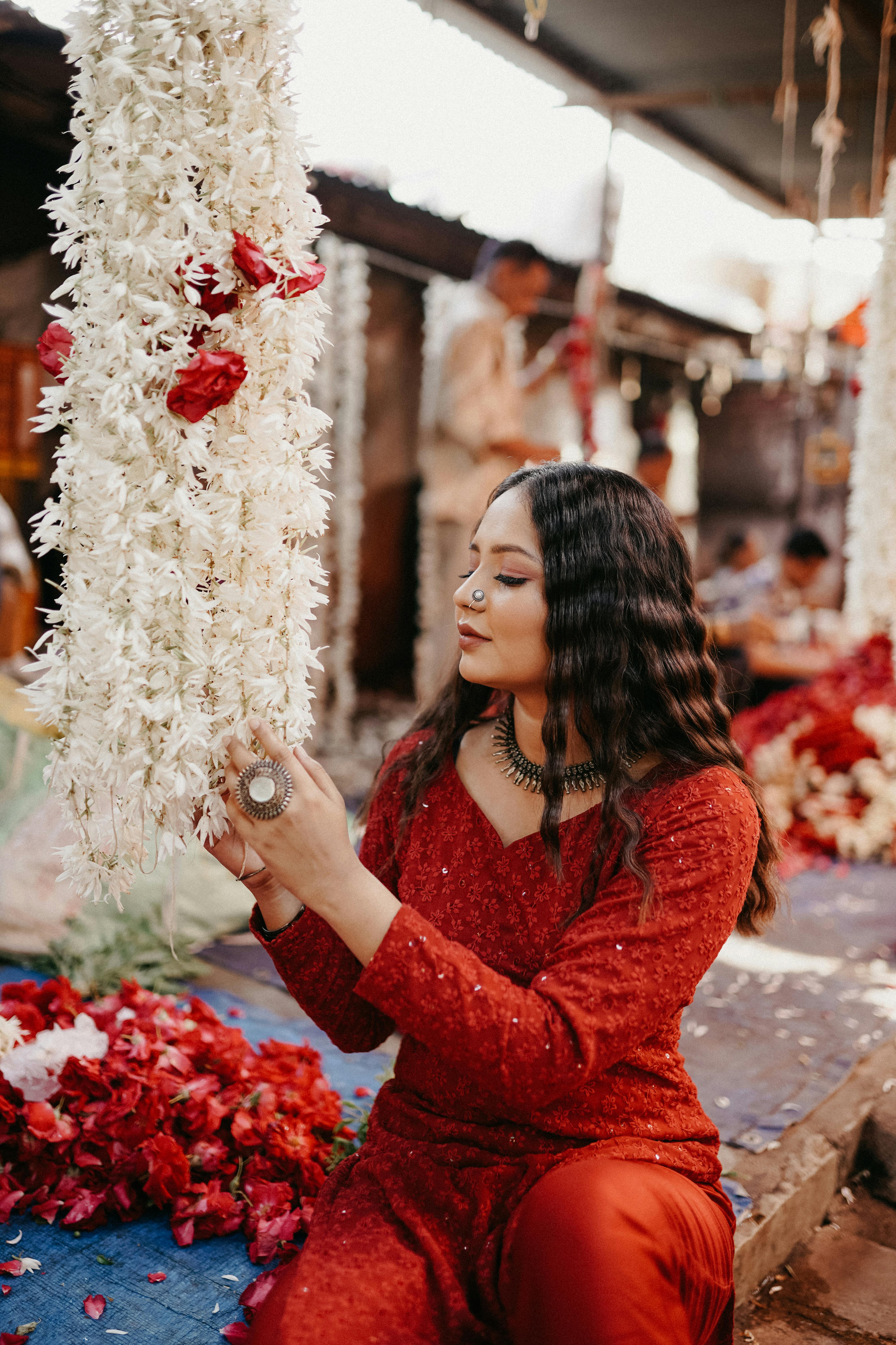 A woman in traditional attire admires a floral garland in a bustling market scene.